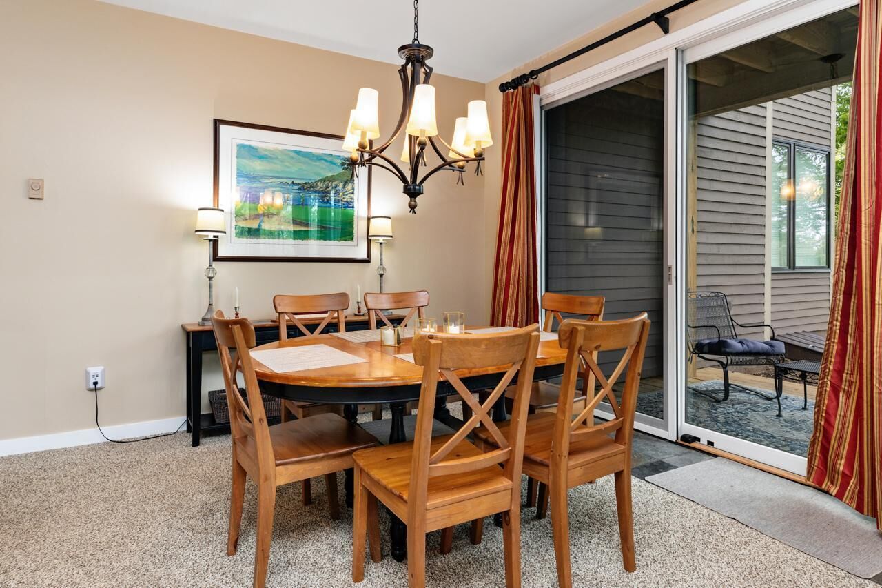 A dining area with a round table, six wooden chairs, a chandelier, a framed painting, and a sliding glass door leading to an outdoor seating area.
