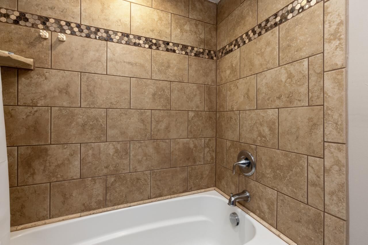 Une salle de bain avec des carreaux de couleur beige, une baignoire blanche et un espace douche.
