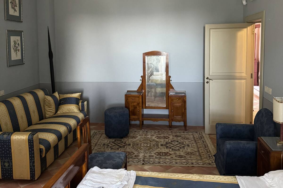 Una stanza con un divano, un letto, una cassettiera, uno specchio e una porta.