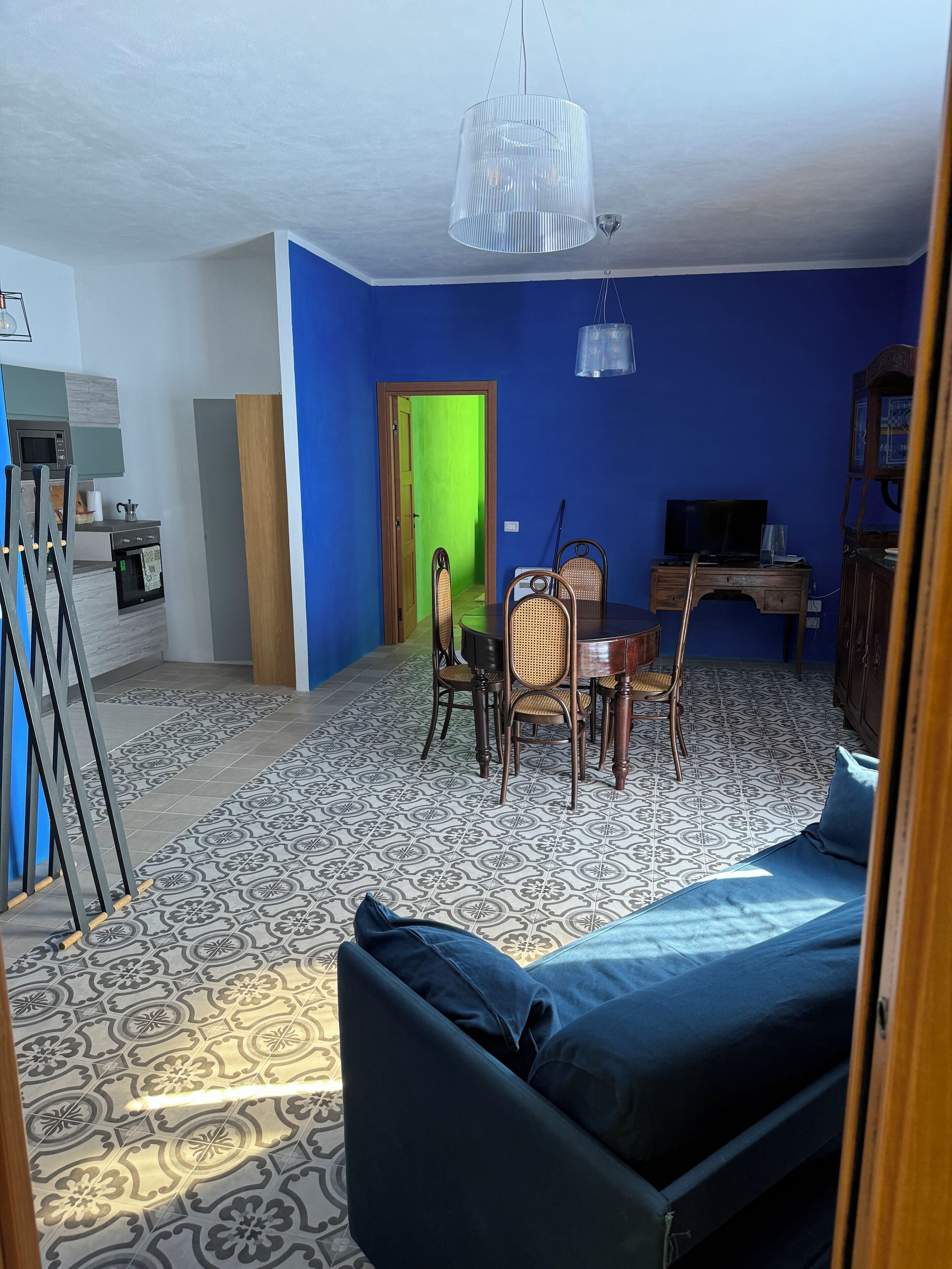 A living room with a blue sofa, a dining table with chairs, a TV, and a kitchen area with a microwave and oven.