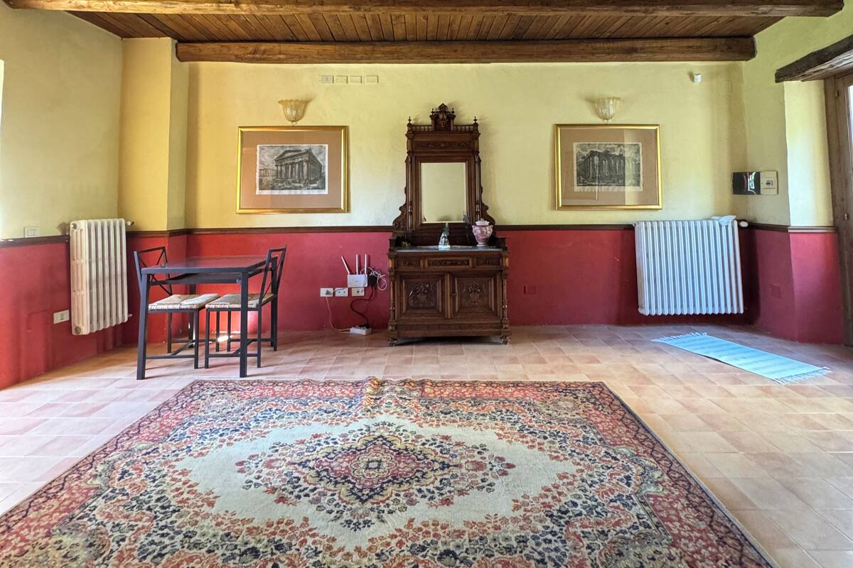 Una stanza con soffitto in legno, un tappeto decorato, un tavolo con sedie e due quadri appesi al muro.
