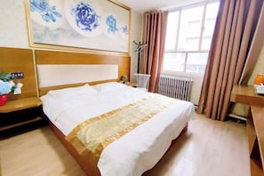 Ein Hotelzimmer mit einem großen Bett, einem hölzernen Kopfteil, einem Fenster mit Vorhängen, einem Heizkörper und einer Wand mit floraler Dekoration.