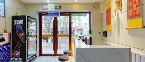 Zona de recepción de hotel con mostrador de mármol, máquina expendedora y puerta de cristal.