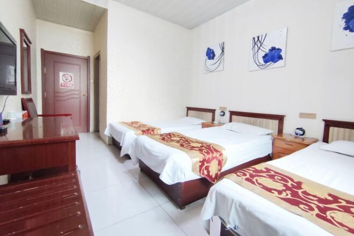 A hotel room with three single beds, a wooden desk, and a television.