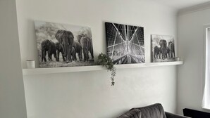 A living room with a grey sofa, a white wall, and three black and white elephant paintings on a shelf. - 3 Bed House - Sleeps 5 - Garden - Parking - Wifi (Dartford)