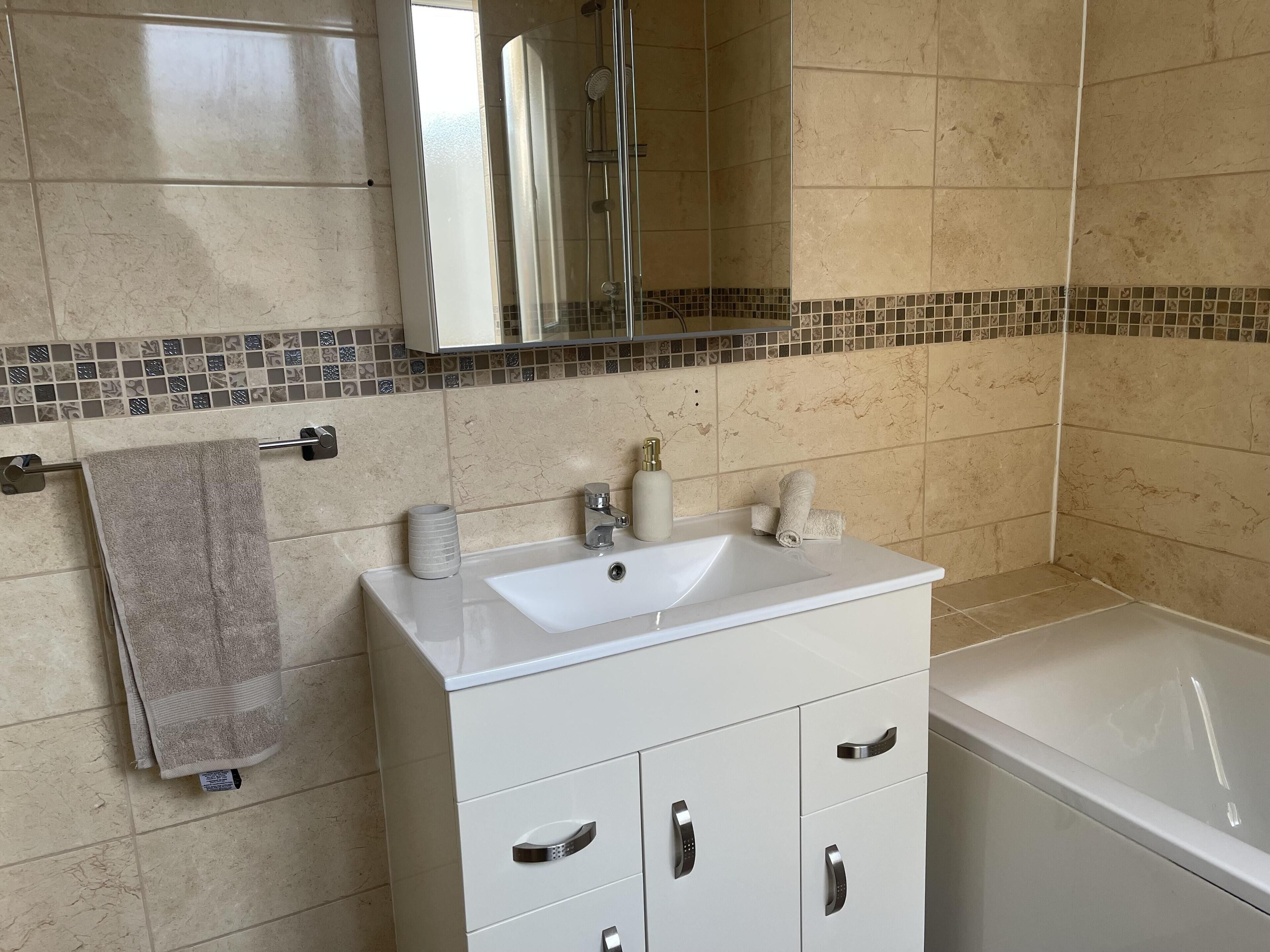 Een badkamer met een wit wastafelmeubel, een wastafel, een spiegel en een bad.