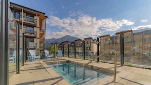 A rooftop pool with clear blue water, surrounded by modern buildings and a mountain in the background. - Mountain Escape | Prime Location | Stunning Views (Canmore)