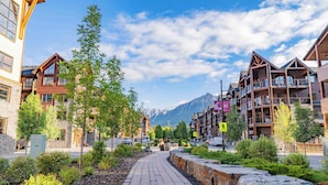 A paved walkway lined with greenery and stone walls, leading to a mountain view. - Mountain Escape | Prime Location | Stunning Views (Canmore)