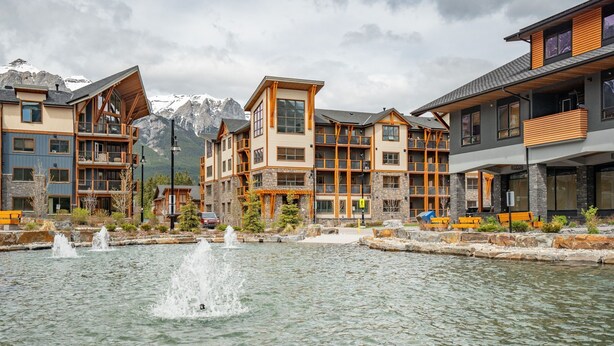 A modern hotel with multiple floors, balconies, and a central water feature. - Mountain Escape | Prime Location | Stunning Views (Canmore)