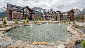A hotel with multiple floors, a central courtyard with a fountain, and a mountain backdrop. - Mountain Escape | Prime Location | Stunning Views (Canmore)