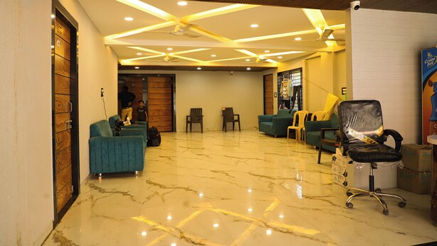 A spacious lobby with a marble floor, wooden ceiling, and a seating area with a blue sofa and chairs. - Hotel Bholenath (Khandwa)