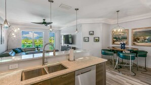 Une cuisine moderne dotée d’un lave-vaisselle intégré, un coin repas avec des chaises vertes et une grande fenêtre offrant une vue sur la verdure.