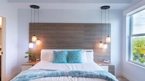 Une chambre moderne avec un lit, un ventilateur de plafond, des luminaires suspendus et une grande fenêtre.