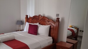 A neatly made bed with a wooden headboard, a bedside table, and a nightstand. - Safari City Two Bedroom Apartment (Nairobi)