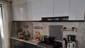 A modern kitchen with a stove, oven, and coffee maker. There are cabinets, a countertop, and a patterned rug. - Safari City Two Bedroom Apartment (Nairobi)
