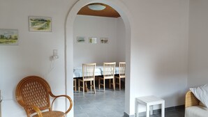A living room with a white sofa, a wicker chair, a dining area with a table and chairs, and a small white side table. - Beautiful town house with room for 5 people close to the center of Nykøbing Mors (Nykøbing Mors)