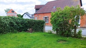 A residential area with a well-maintained lawn, a hedge, and a brick house with a red roof. - Beautiful town house with room for 5 people close to the center of Nykøbing Mors (Nykøbing Mors)