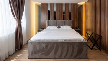Una habitación de hotel moderna con una cama grande, paredes de paneles de madera, una mesita de noche y una silla de respaldo cruzado.