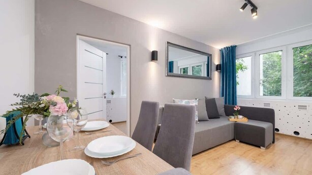 A modern living room with a dining area, grey sofas, and a large window with curtains. - Comfortable Apartment for 4 people | Close to Tauron Arena (Kraków)