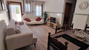Ein Wohnzimmer mit einer Couch, einem Esstisch mit Stühlen, einem Fernseher und einer Pflanze.