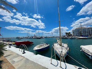 Un port de plaisance où sont amarrés différents types de bateaux, un ciel dégagé et un bâtiment en arrière-plan.