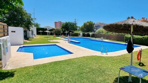 Ein Schwimmbecken mit Sprungbrett und Rettungsring, umgeben von Gras und einem Strohdachschirm.
