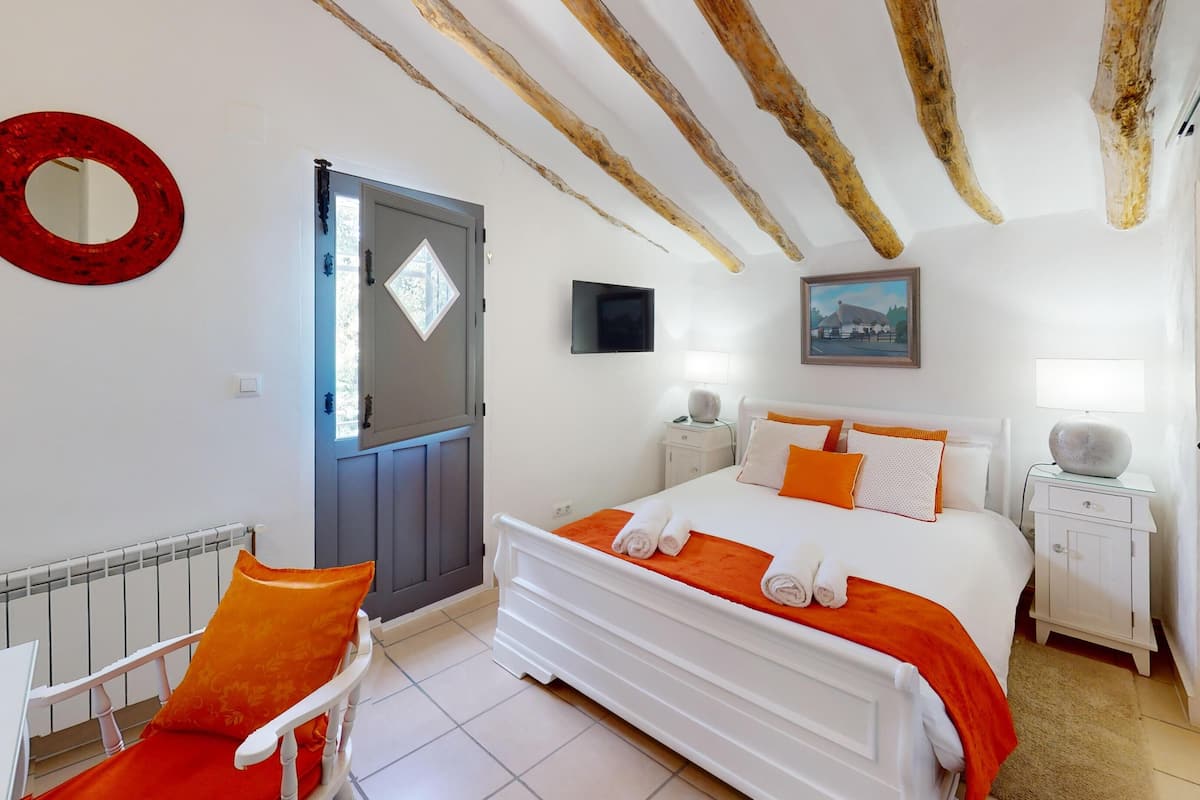A bedroom with a bed, a chair, a bedside table, a mirror, and a door.