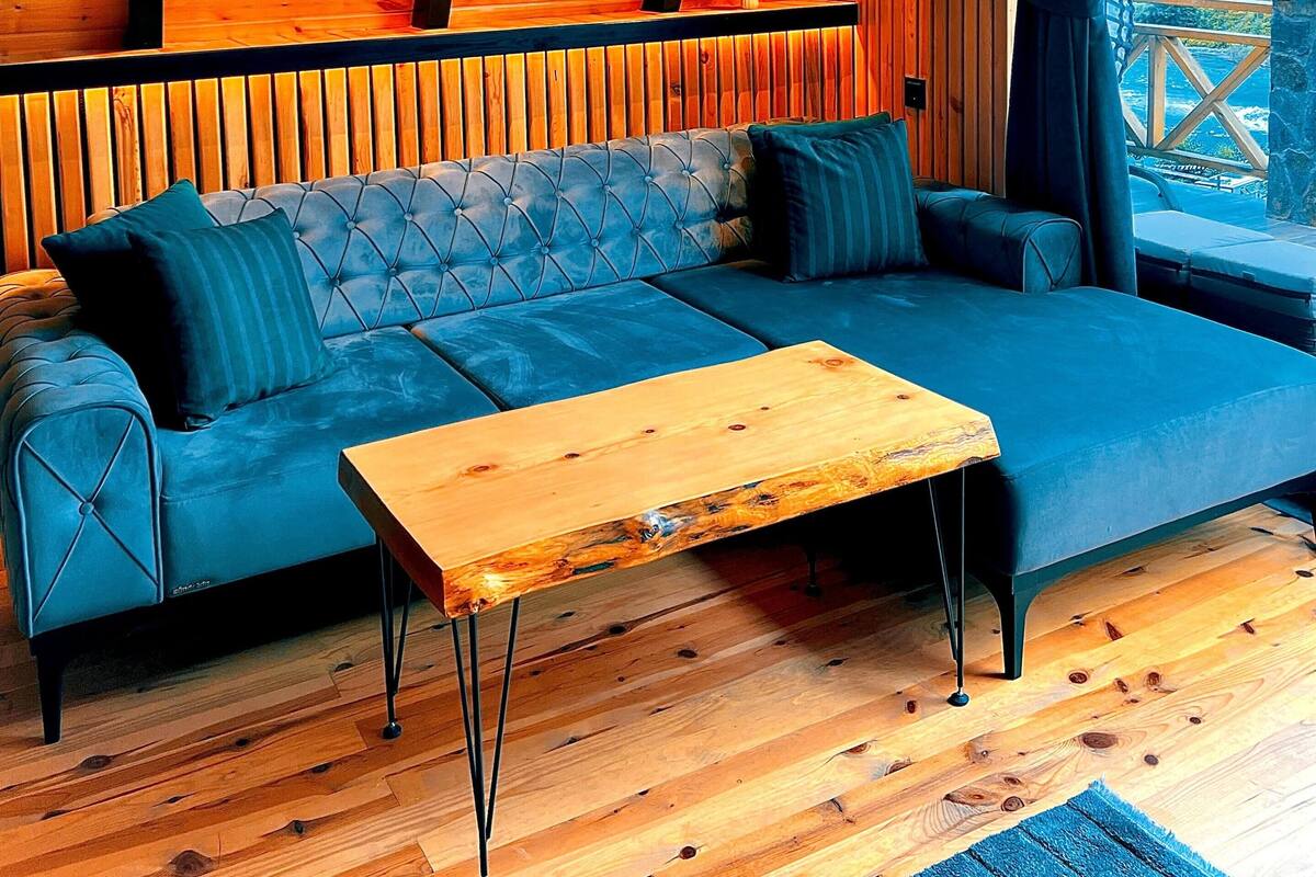 Une pièce chaleureuse avec un plafond en bois, un canapé bleu, une table basse en bois et une vue sur l’extérieur.