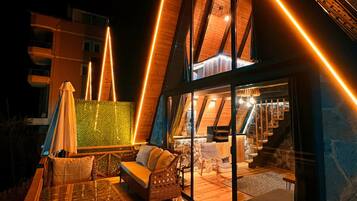 A modern loft-style room with a glass door leading to a balcony, furnished with wicker furniture and a glass table.