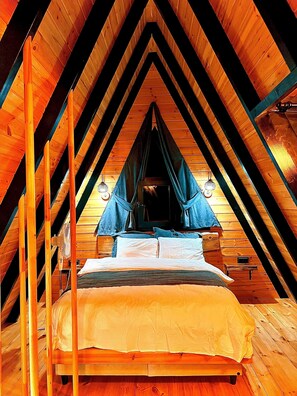 A wooden loft bedroom with a sloped ceiling, a bed with a blue canopy, and a small table. - Mirana Bungalov (Ardesen)