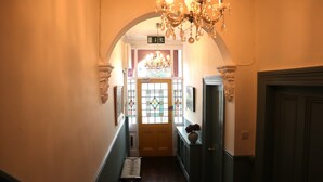 A hallway with a bench, a chandelier, and a door with stained glass.