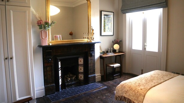 A bedroom with a fireplace, a large mirror, a bed, and a window with curtains.