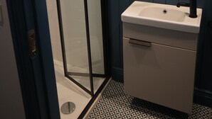 A bathroom with a glass shower enclosure, a white sink with a black faucet, and a window above the sink.