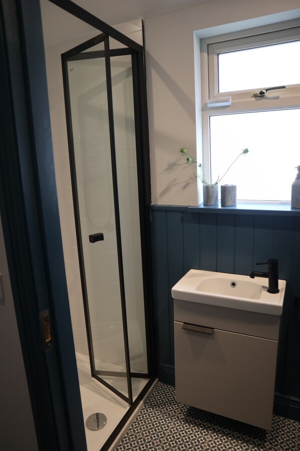 Un baño con cabina de ducha de vidrio, un lavamanos blanco con grifo negro y una ventana sobre el lavamanos.