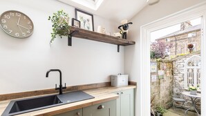 A kitchen with a wooden countertop, a black sink, and a green cabinet. There is a clock on the wall and a shelf with decorative items. - Host Stay Arundel Cottage (Whitby)