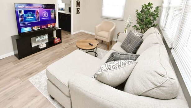 A living room with a beige sofa, a coffee table, a TV on a stand, and a small plant. - 5 min Walk to Notre Dame Modern Home 517 (South Bend)