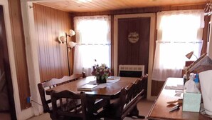 A dining area with a wooden table and chairs, a vase with flowers, and a desk with a lamp and a tissue box. -  Farmhouse sleeps 2 -6  in the Allegheny National Forest outside Bradford Pa (Bradford)