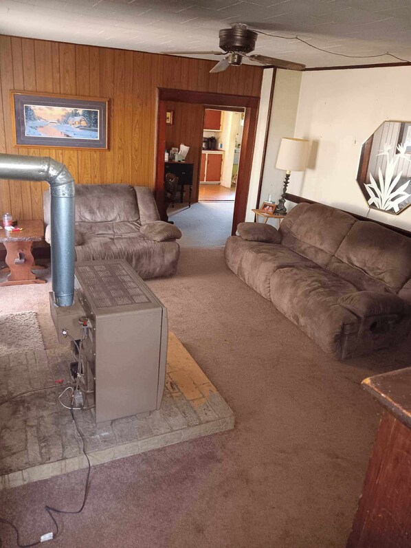 A living room with two brown sofas, a wooden wall, a ceiling fan, and a fireplace with a metal pipe.