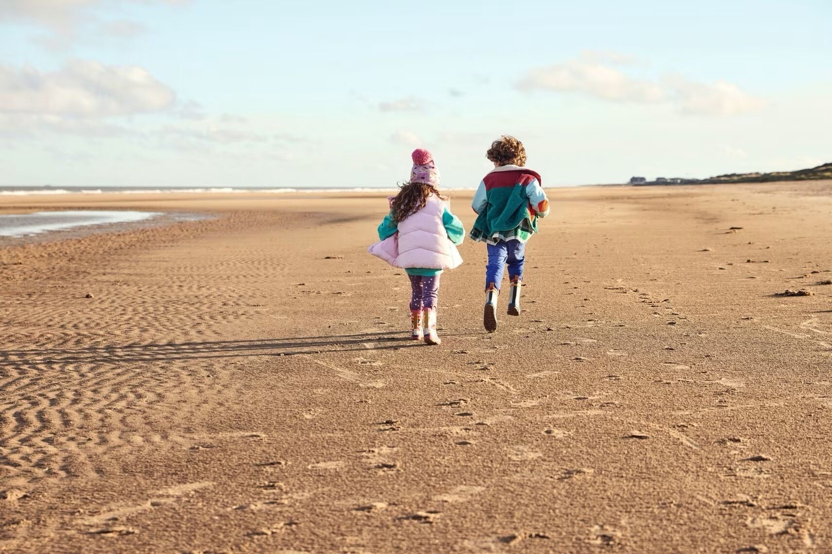 Two children walking on a sandy beach with footprints.