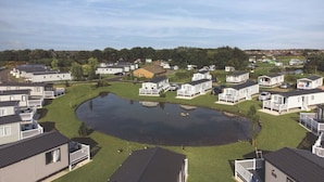 A mobile home park with several single-story homes, a central pond, and a grassy area. - Mablethorpe Lakeside Caravan With Decking & Wi-fi! (Mablethorpe)