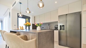 A modern kitchen with a large island, stainless steel appliances, pendant lighting, and a view of the living area. - Villa Oasis (Trogir)