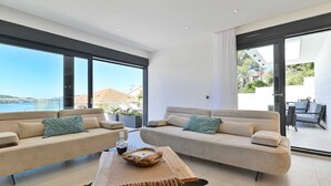 A modern living room with two sofas, a coffee table, and large windows offering a view of the sea and buildings. - Villa Oasis (Trogir)