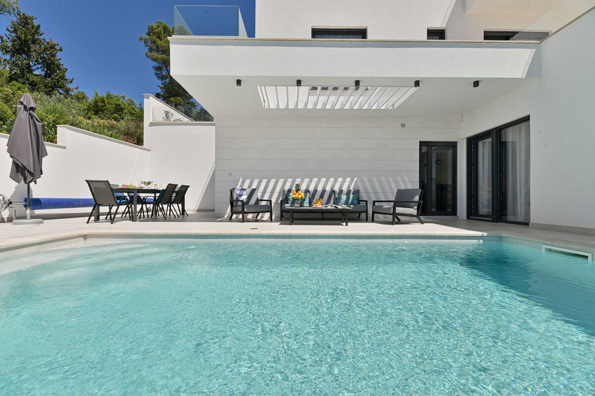 A modern outdoor pool area with a seating arrangement and a covered patio.