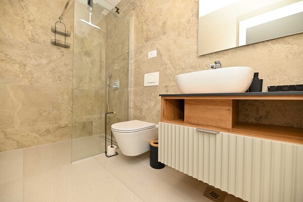Un baño moderno con cabina de ducha de vidrio, inodoro blanco, tocador de madera y un espejo grande.
