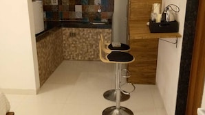 Eine kompakte Küche mit ornamental gestalteter Spritzschutzwand, einer Holztür, einem kleinen Barhocker und einer Arbeitsplatte mit einem Glasbehälter.