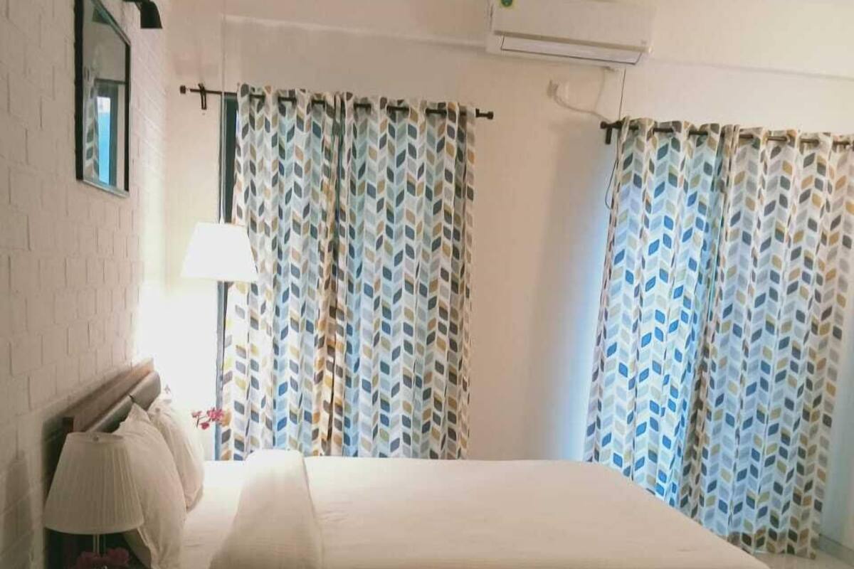 A bedroom with a bed, a nightstand, a lamp, a ceiling fan, and patterned curtains.