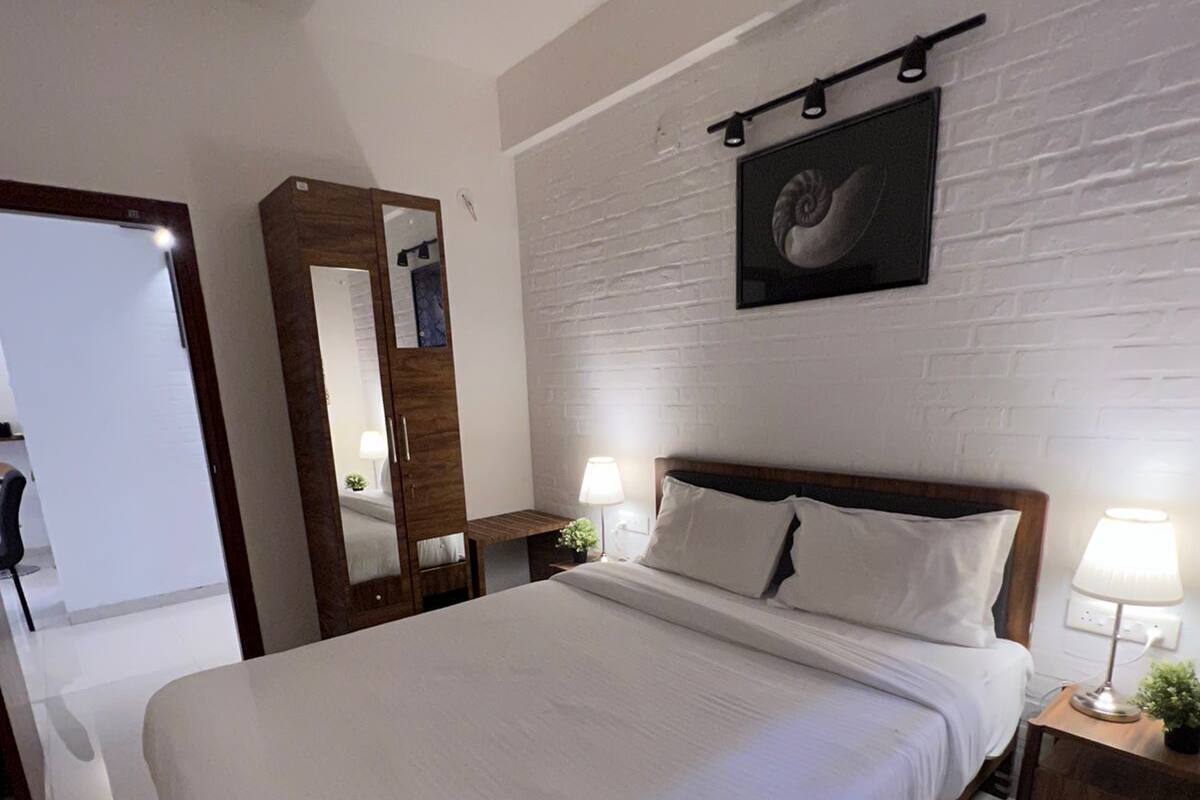 A modern bedroom with a large bed, a wooden wardrobe, a mirror, and a wall-mounted picture.