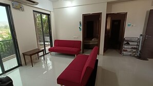 Ein geräumiger Wohnbereich mit einem roten Sofa, einem kleinen Tisch und einem Balkon mit Aussicht.