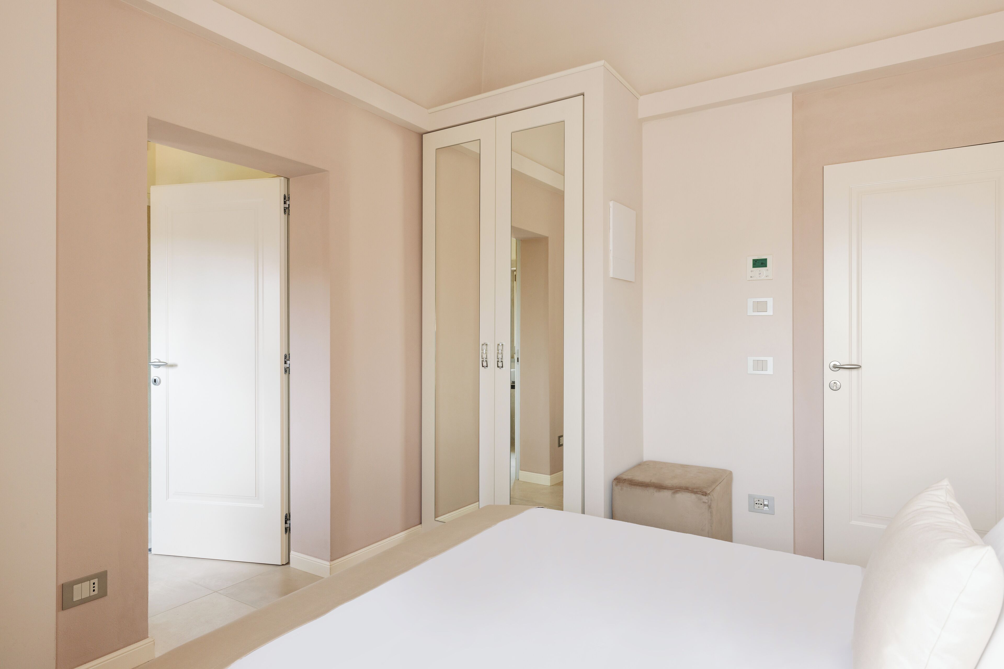 A bedroom with a bed, a small stool, a wardrobe, and a door leading to another room.