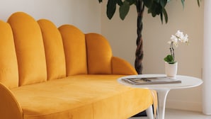 A mustard-colored sofa with white legs, a white round table with a clear glass top, and a potted plant with white flowers. - Prato dei Miracoli Residenza d'Epoca (Pisa)